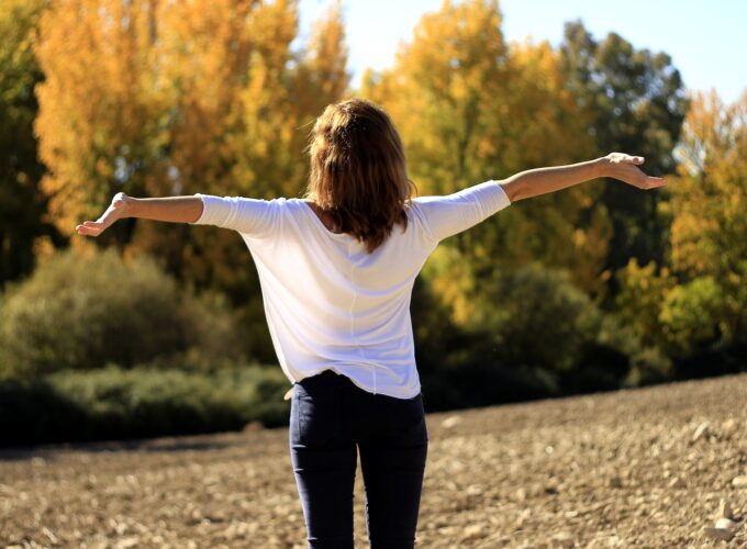 Femme debout, les bras grands ouverts, respirant profondément en pleine nature par une journée ensoleillée