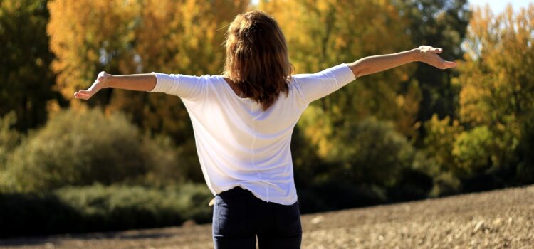 Femme debout, les bras grands ouverts, respirant profondément en pleine nature par une journée ensoleillée