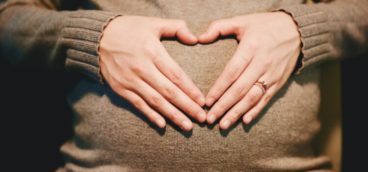 femme enceinte posant ses mains à plat en forme de cœur sur son ventre – le massage pendant le premier trimestre de grossesse