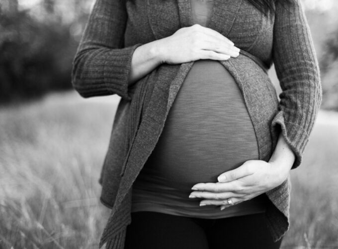 Une femme dont la grossesse est bien avancée se tient debout, la main droite et la main gauche respectivement au sommet et à la base du ventre