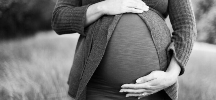 Une femme dont la grossesse est bien avancée se tient debout, la main droite et la main gauche respectivement au sommet et à la base du ventre