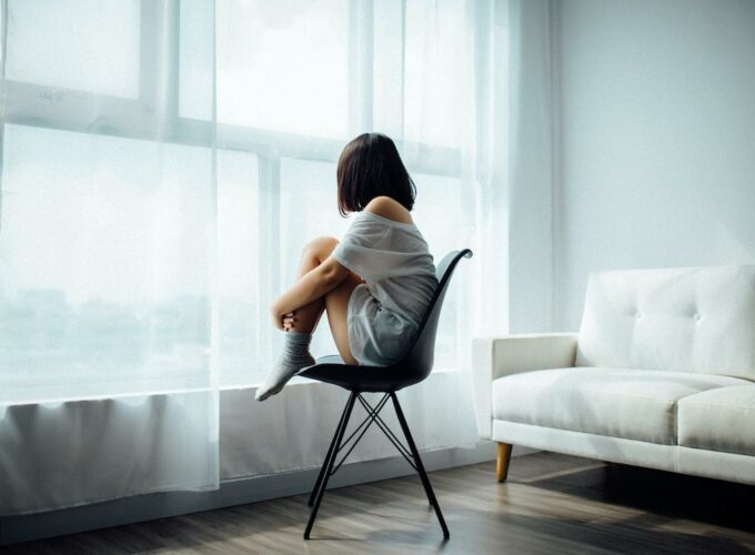 Jeune femme assise, que l’on devine triste ou déprimée, regardant par la fenêtre.
