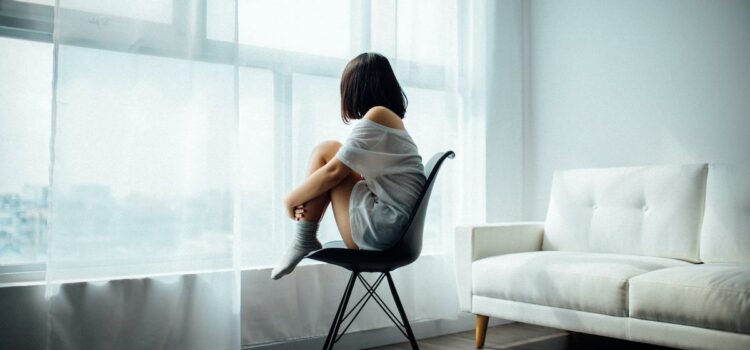 Jeune femme assise, que l’on devine triste ou déprimée, regardant par la fenêtre.
